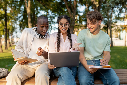 Three friends are enjoying a study session in a park, engaged in lively conversation. They share ideas while using a laptop, surrounded by greenery.