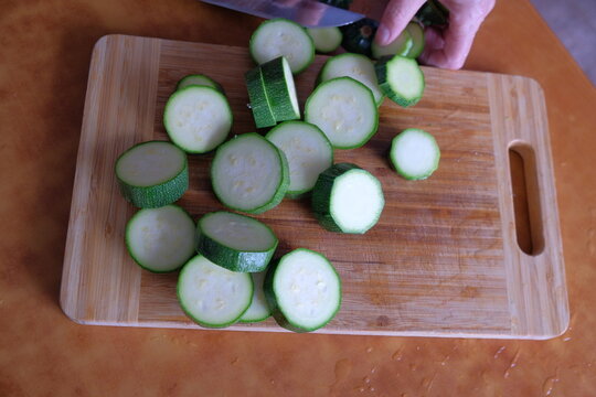 A woman and a man fry zucchini in a frying pan in an apartment in the dark evening light. sliced cucumber on a cutting board