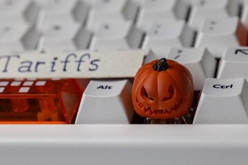 scary jack-o'-lantern keycap sits on a clean mechanical keyboard, next to an orange shift key and a paper tag with the word 'tariffs,' symbolizing trade issues