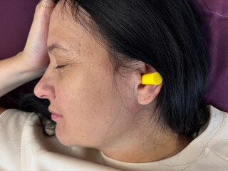 Fototapeta premium Close up of adult brunette woman sleeping with yellow earplugs, noise protection for healthy sleep, deep rest, insomnia prevention and peaceful home bedroom atmosphere