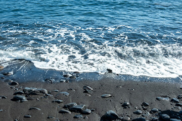 Black Volcanic sand beach and blue water ocean in Madeira, coast Portugal, Atlantic waves sparkle in sun, warm Gulf Stream water flows, peaceful energy, marine life