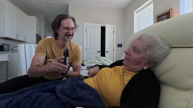 An elderly woman enjoys a heartfelt conversation with her son while they spend quality time together in a nursing home setting.