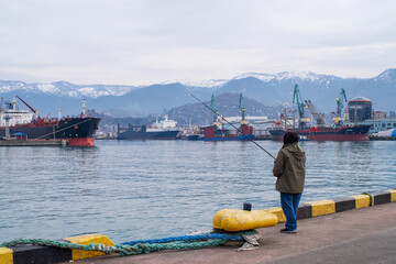 A fisherman fishes in the port of Batumi on a winter day in January.	