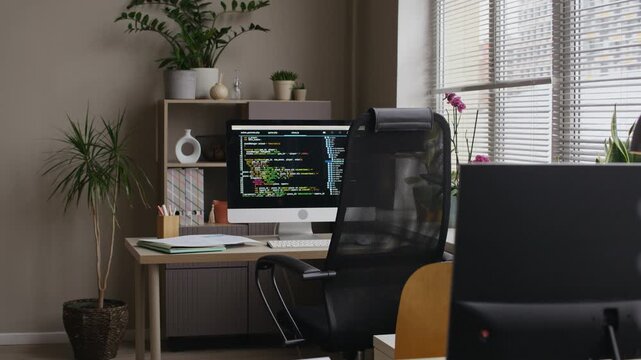 Long shot of modern office workspace with coding screen on computer monitor on table with documents