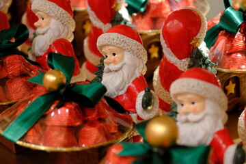 Christmas chocolates with Santa Claus figures. Gift chocolates with red packaging, green ribbons, and yellow balls. Happy New Year. Welcome 2026. Merry Christmas.