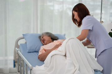 Fototapeta premium Asian nurse helping a senior Asian female patient with stomach ache on a bed in hospital