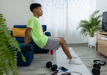 Young man doing tricep dips in his living room, with hands on a pouf and feet on a mat. Home workout routine focused on strength and well being