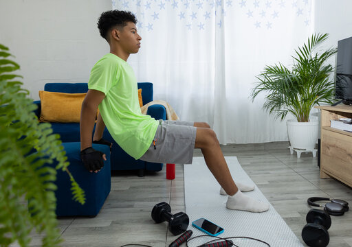 Young man doing tricep dips in his living room, with hands on a pouf and feet on a mat. Home workout routine focused on strength and well being