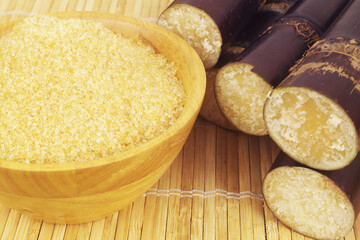 Brown sugar in bowl and sugar cane sticks on bamboo background