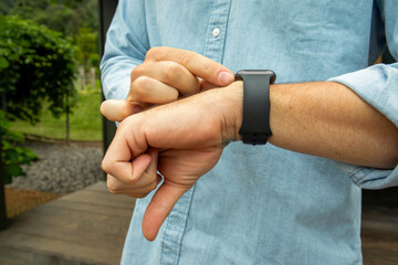 Man adjusting smartwatch while standing outdoors in a farm area