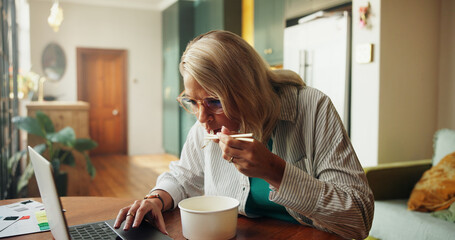 Woman, remote work and food with laptop at house for lunch break, multitasking and interior design. Female person, pc and eating noodles with fabric swatches, renovation research and home improvement