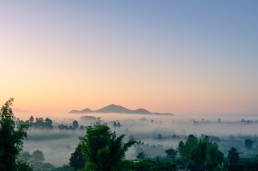 A beautiful winter view of morning light streaming down through the mist, mountains, trees and rice fields in rural Chiang Rai Province, Northern Thailand.