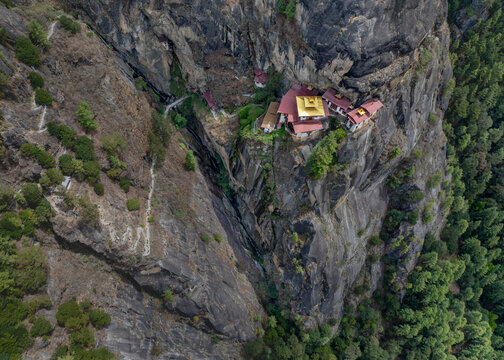 Aerial view of the Taktsang Monastery perched dramatically on a cliffside, a jewel amidst the rugged terrain and emerald forests, Paro, Paro, Bhutan.