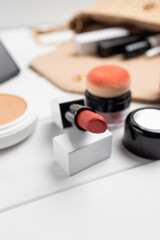 Red lipstick, powder and open handbag with makeup products on white wooden background, beauty essentials and cosmetics concept