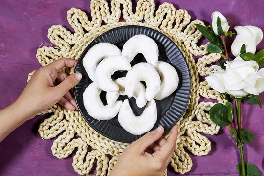 Oriental Algerian sweet cookies named tcharek aryen in arabic which mean almond cookies in english  On Black Plate With Hands, Rustic Woven Mat And White Roses 