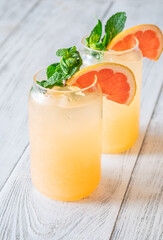 Two chilled Paloma cocktails with grapefruit slices and mint sprigs on white wood