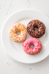 Pink white and chocolate glazed donuts arranged neatly on clean minimalist white plate