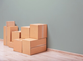 A pile of plain brown cardboard moving or storage boxes sits on a light wooden floor against a...