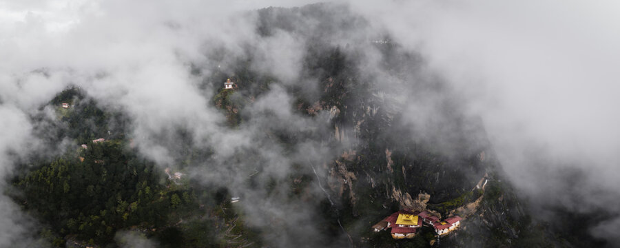 Aerial view of Tigers Nest monastery clinging to a steep cliff face, shrouded in ethereal mist, a golden beacon amidst the rugged terrain, Paro, Bhutan.