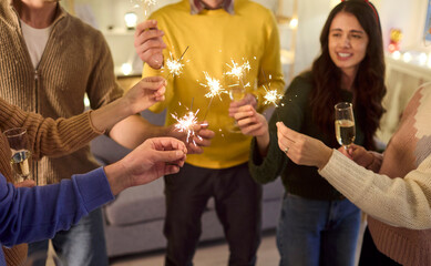 Sparklers and friends toast champagne flutes. Warm hands gather as bright sparks crackle and...