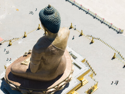 Aerial view of the Great Buddha Dordenma statue, its golden hue contrasting against the vast concrete plaza where tiny figures stroll, Thimphu, Bhutan.