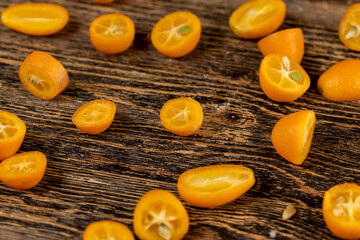 lots of ripe orange kumquat cut in half on a wooden table, a group of scattered and sliced kumquat fruits on a wooden table and board