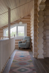 A chair on the mezzanine floor near the window provides a second light. Interior of the second floor of a log house made of northern pine.