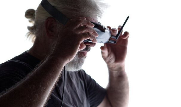 silhouette of bearded elderly man operating FPV drone in googles on his head, studio shot of man and modern technologies