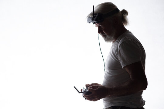 Silhouetted elderly man operating racing drone in goggles and remote control on a white isolated background, modern hobby and technology