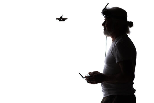 Silhouetted elderly man operating racing drone in goggles and remote control on studio background, modern hobby and technology