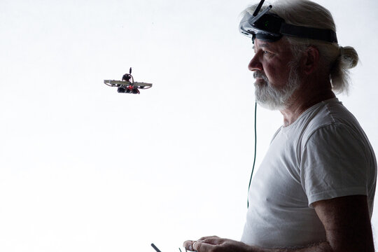 Silhouetted elderly man operating racing drone in goggles and remote control on studio background, modern hobby and technology