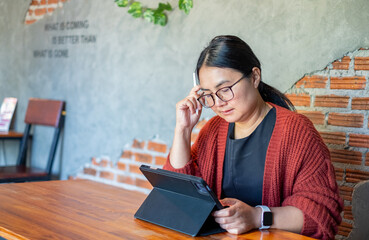 A woman working on a digital tablet with a stylus in a calm workspace. She focuses on creative tasks at a wooden desk, showing modern technology use and remote work lifestyle.