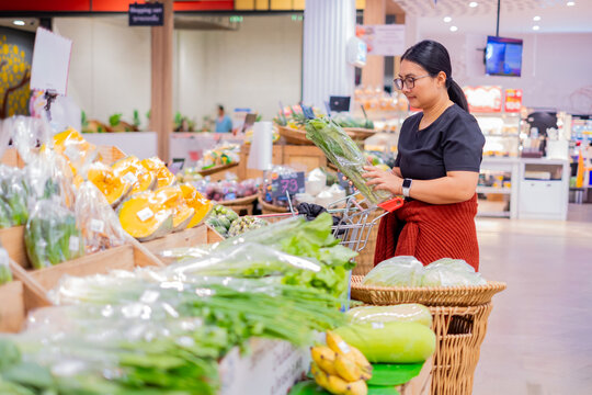 A woman shopping for fresh vegetables at a supermarket, carefully selecting produce and placing items into her cart, representing healthy living, grocery shopping, and everyday lifestyle choices.
