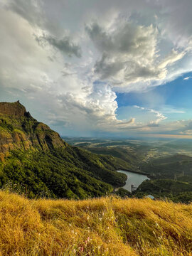 Breathtaking view from Konkan Kada in Bhandardara with lush green mountains, golden grass, dramatic monsoon clouds, and a serene valley reservoir in Maharashtra, India.