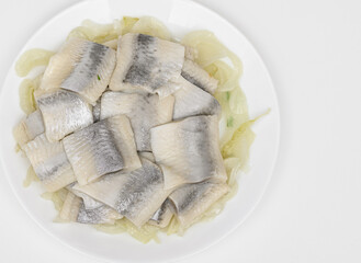 Pieces of marinated herring in oil with onion on a plate