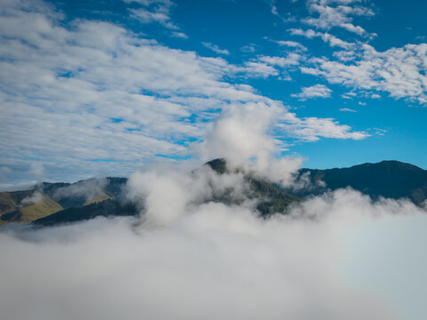 Aerial view of a sea of clouds partially obscuring the lush, undulating hills of the Phobjikha Valley under a bright blue sky, Nubding, Wangdue Phodrang, Bhutan.
