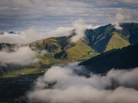 Aerial view of the Phobjikha Valley, where green meadows meet the sky, and clouds dance among the rolling hills, Nubding, Wangdue Phodrang, Bhutan.
