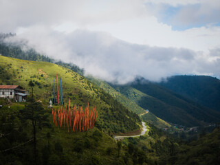 Aerial view of prayer flags fluttering vibrantly against the verdant slopes of Pelela Pass under a sky draped with soft clouds, Black Mountain range, Wangdue Phodrang, Bhutan.