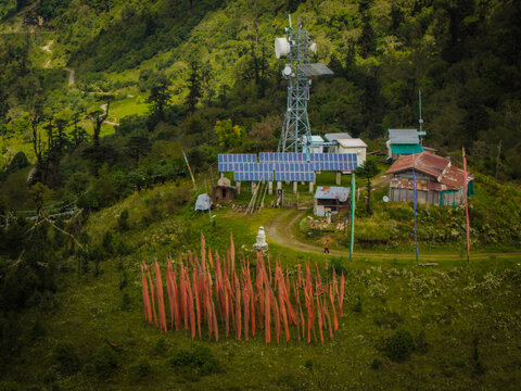 Aerial view of prayer flags flutter against the backdrop of a telecommunications tower and solar panels, Pelela Pass, Wangdue Phodrang, Bhutan.