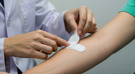 Doctor applying adhesive bandage to patient's arm in medical setting  
