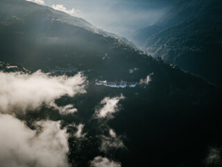 Aerial view of a majestic fortress perched atop a mountain ridge, shrouded in ethereal clouds and bathed in the soft glow of sunlight, Trongsa, Trongsa, Bhutan.