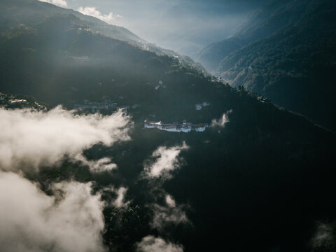 Aerial view of a majestic fortress perched atop a mountain ridge, shrouded in ethereal clouds and bathed in the soft glow of sunlight, Trongsa, Trongsa, Bhutan.