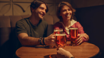 Young people cheering beer glasses with bright bar lights. Concept of youth nightlife culture, bar marketing, brewery content, celebratory weekends, and vibrant social experiences.