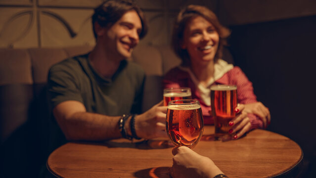 Young people cheering beer glasses with bright bar lights. Concept of youth nightlife culture, bar marketing, brewery content, celebratory weekends, and vibrant social experiences.