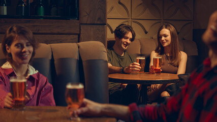 Friends enjoying beer together in relaxed pub corner. Concept of cozy bar visuals, lifestyle branding, brewery storytelling, casual socializing, and warm evening leisure scenes.