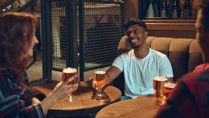 Friends chatting with beer glasses at wooden pub table. Concept of bar lifestyle content, brewery...