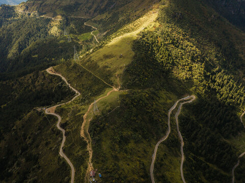 Aerial view of winding roads carve through the rugged terrain of Chele La Pass, where sunlight dapples the landscape, Paro, Paro, Bhutan.