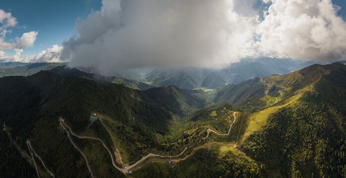 Aerial panoramic view of winding roads cutting through the lush green mountains, partially veiled by a thick blanket of clouds, Chele La pass, Paro, Bhutan.