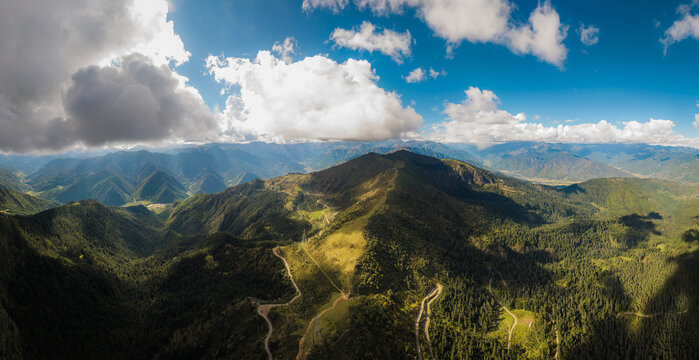 Aerial panoramic view of the Chele La pass, where shadows dance across the rolling green mountains under a vibrant blue sky, Paro, Paro, Bhutan.