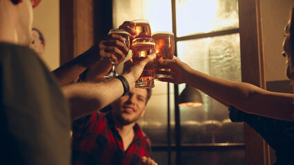 Friends cheering beer glasses in evening pub atmosphere. Concept of nightlife promotion, brewery advertising materials, bar culture storytelling, and beverage-focused marketing